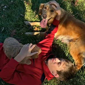 Boy laying down with puppy on his chest while petting the mama dog
